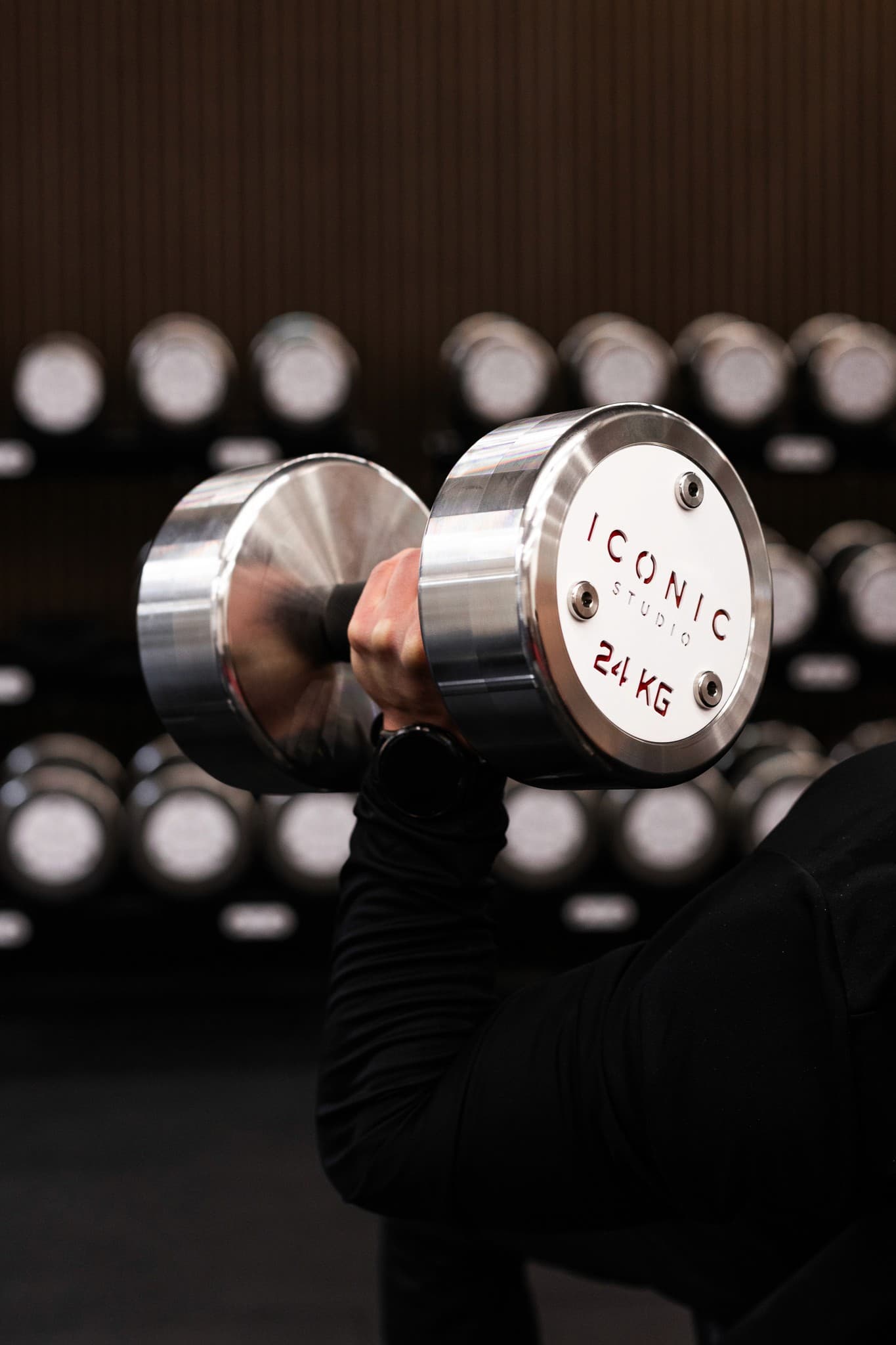 Iconic Studio custom chrome 24 kg dumbbell — branded equipment, full rack in background